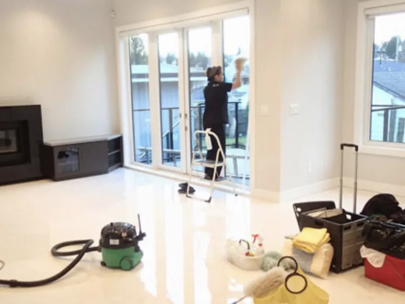 Cleaner dusting the tall windows of a large living room